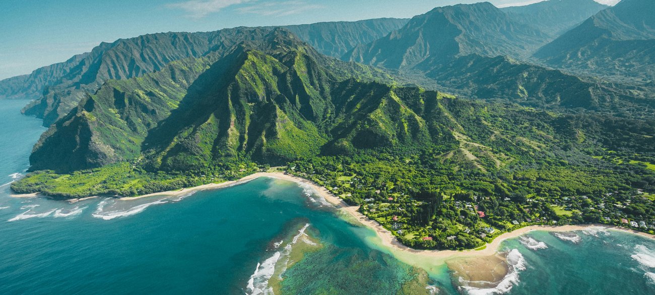 Aerial view of the dramatic cliffs of the Na Pali Coast and pristine beaches in Kauai, Hawaii, showcasing stunning natural beauty and vibrant greenery.