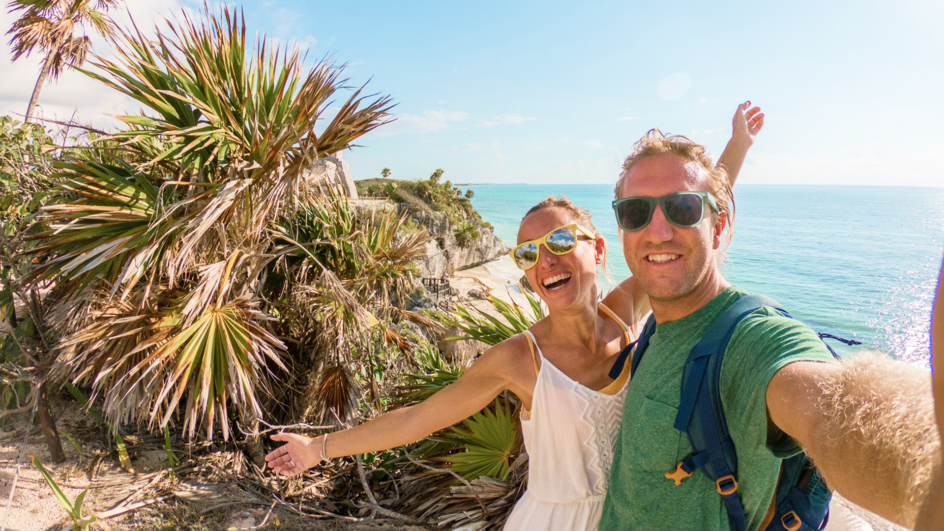 Couple taking a selfie atop ancient coastal ruins overlooking turquoise Caribbean waters in Cancún