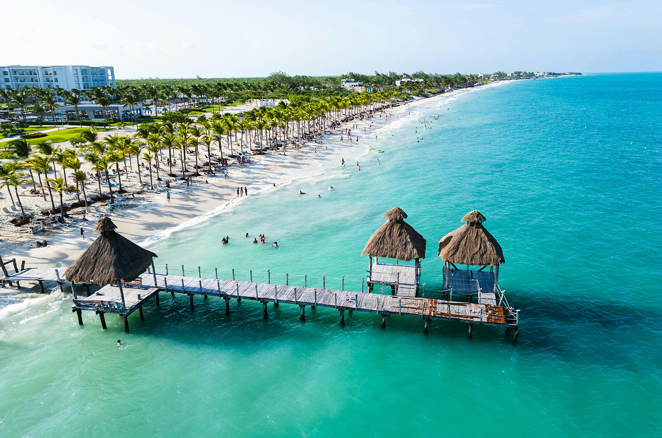 Wooden pier with palapa-roofed gazebos stretching into the turquoise sea at Playa Mujeres beac