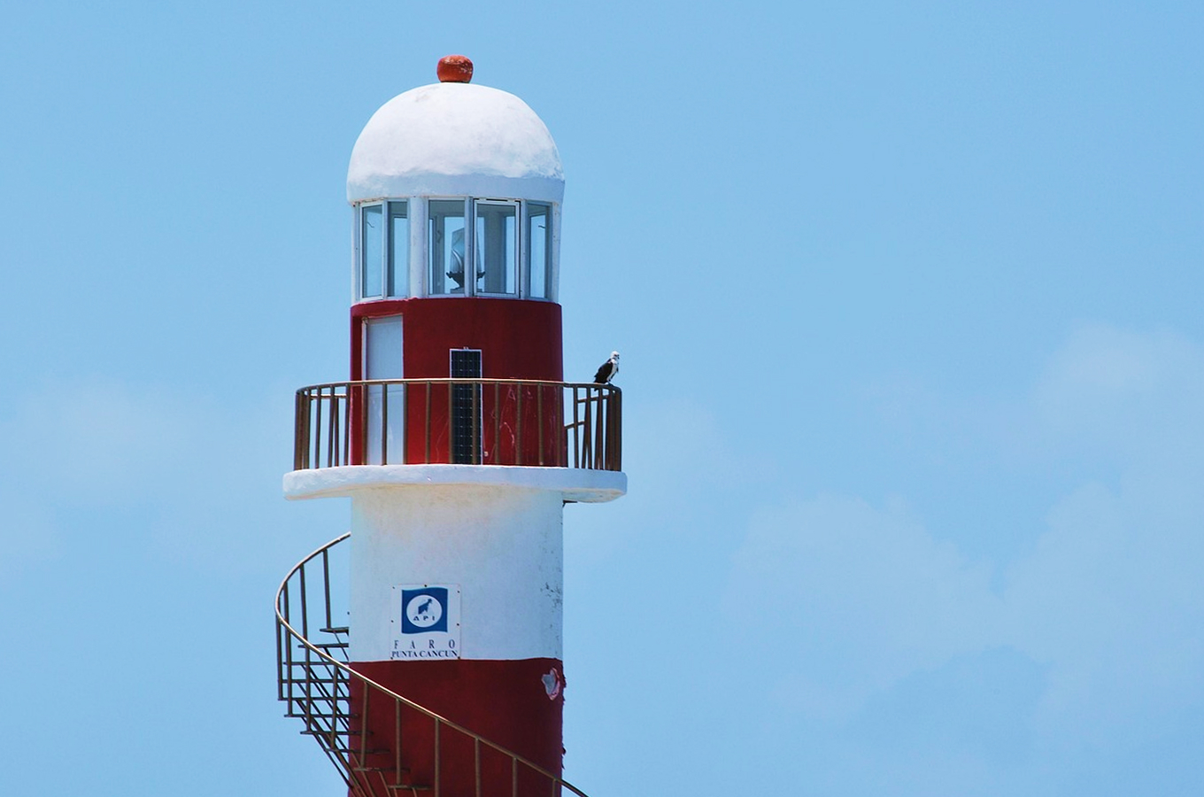Red and white Faro Punta Cancún lighthouse with spiral staircase standing against a bright blue sky