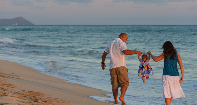 young couple with their daughter walking in the water at Nimitz Beach on a warm sunset with Diamond Head in the background.
