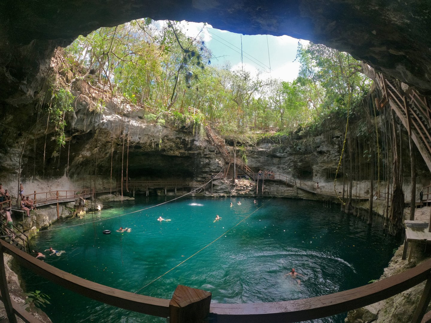 Travelers swimming in a cenote cave near Tulum surrounded by limestone cliffs and jungle